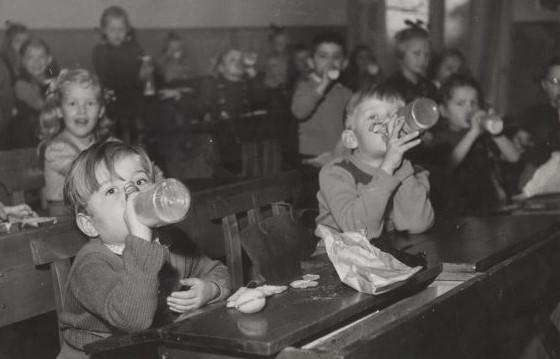 Lapset juovat maitoa pulloista koululuokassa 1900-luvun puolivälissä.